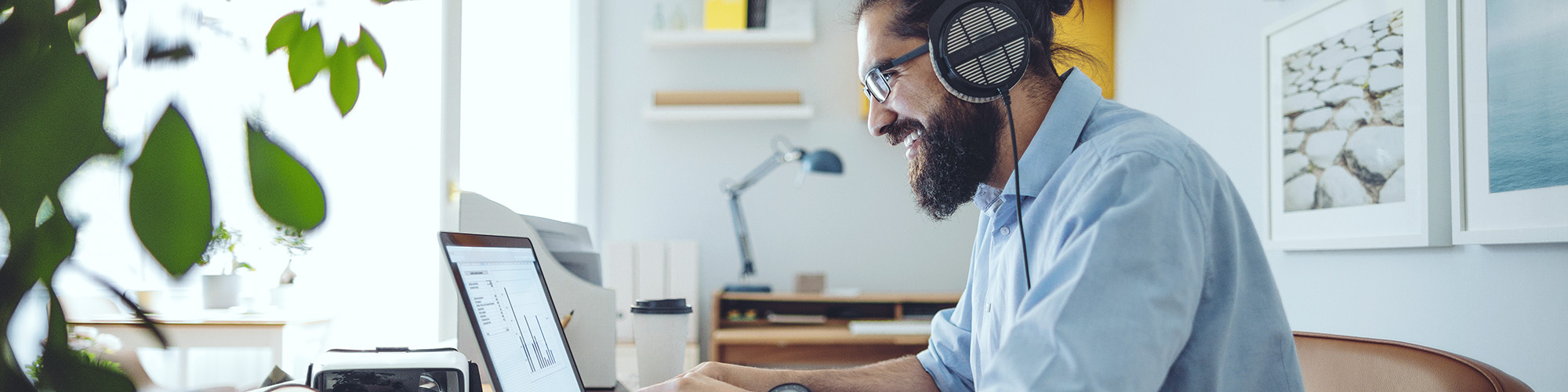 A man is sitting at his desk in front of a laptop