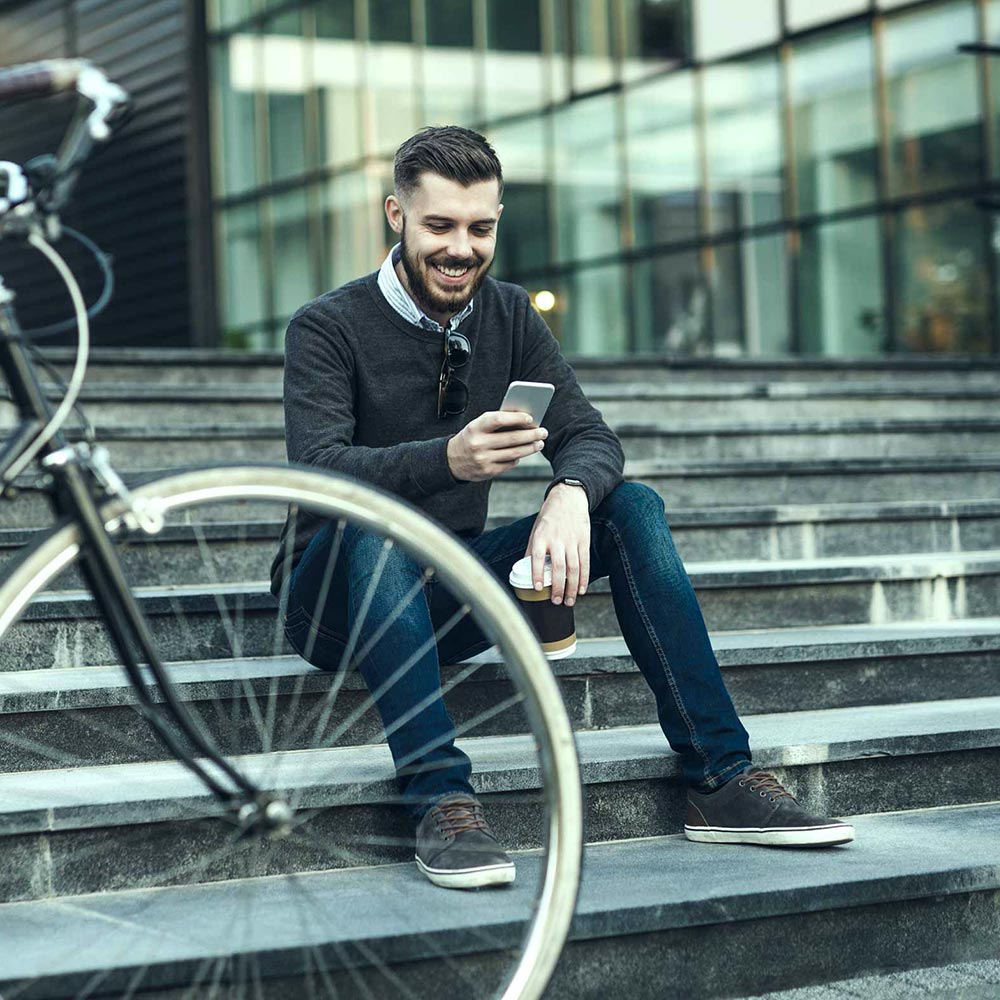 Jeune homme assis dans les escaliers regarde son téléphone cellulaire en souriant