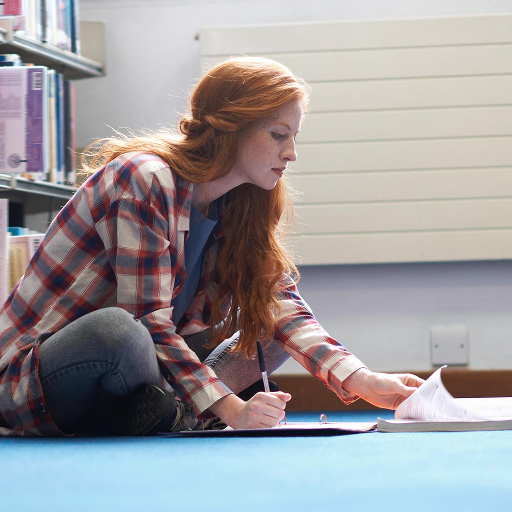Étudiante assise par terre dans une bibliothèque