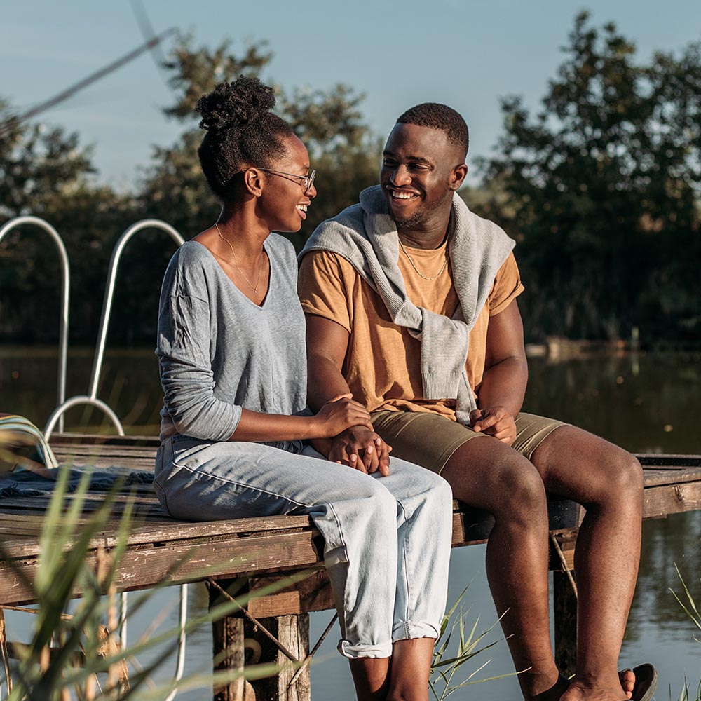 Jeune couple sourit assis sur un quai