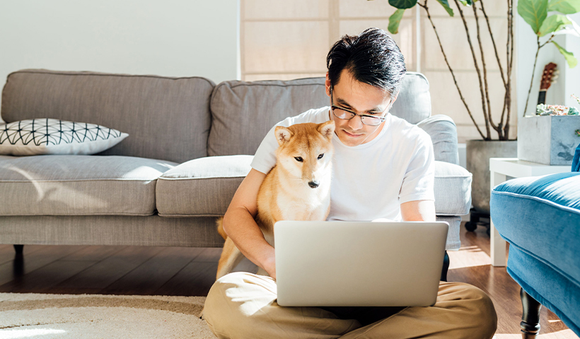 Homme assis au sol avec son chien devant son ordinateur portable